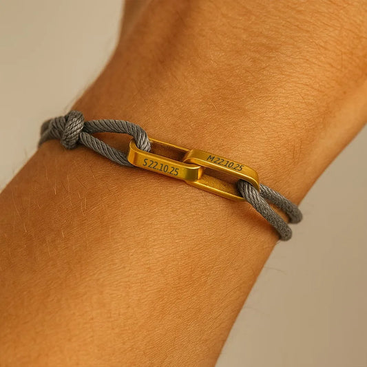 Koppelarmband met grijs koord en twee gouden schakels om een pols
